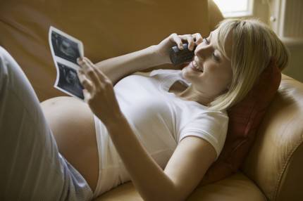 donna incinta  sorridente osserva l'ecografia del suo bambino 