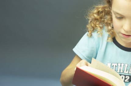 Bambina di 6 anni legge attentemente un libro rosso