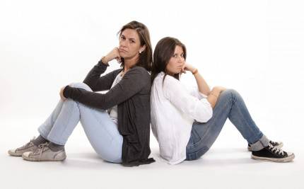 mamma e figlia adolescente sedute per terra si danno le spalle