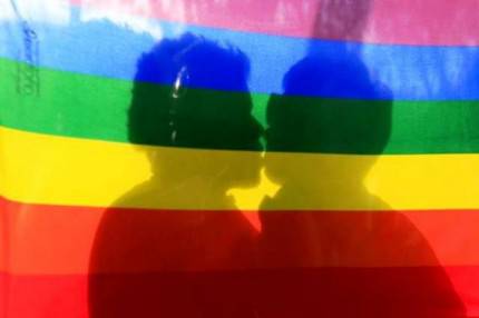 L'ombra di due ragazzi che si baciano si vede attraverso una bandiera arcobaleno
