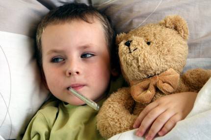 Un bimbo è a letto e misura la febbre mentre stringe il suo orsacchiotto