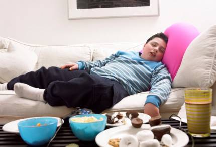 ragazzo grasso sul divano con davanti schifezze da mangiare