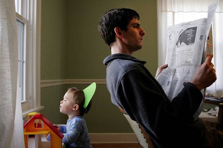padre e figlio di spalle, uno legge il giornale, l'altro guarda dalla finestra