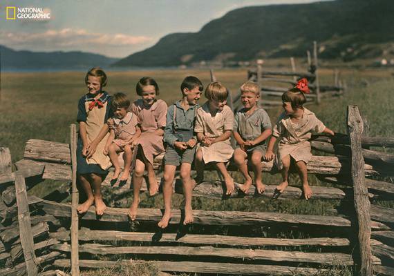 sette bambini seduti su una staccionata in paesaggio campestre