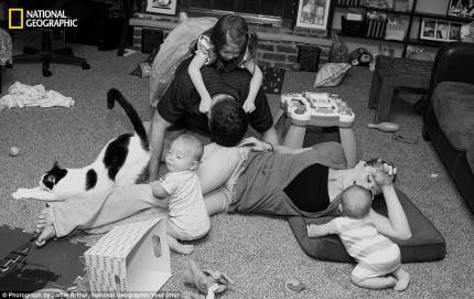 famiglia composta da madre padre ftre figli e gatto ripresa in bianco e nero distesi sul tappeto a giocare