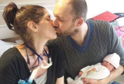 uomo bacia danna in letto di ospedale tenendo in braccio la loro piccola appena nata