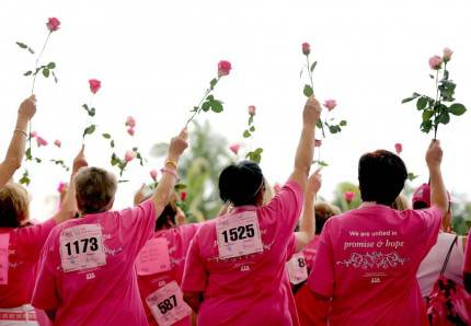 donne di spalle indossano tshirt rosa simbolo lotta tumore al seno e tengono in mano una rosa rivolta verso l'alto