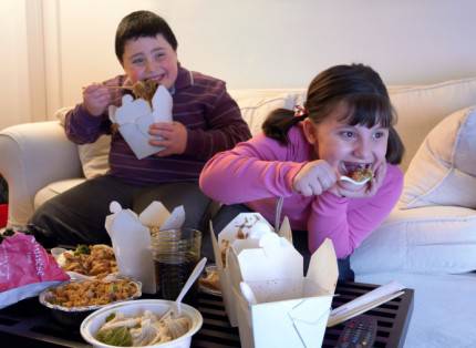fratello e sorella in sovrappeso seduti sul divano davanti alla tv mangiano cibo da asporto